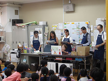 写真：学童で子供たちの前で紙芝居のような資料を読み聞かせている様子