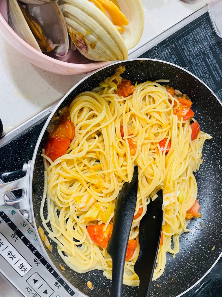 パスタとねぎとトマトをフライパンで絡めている画像