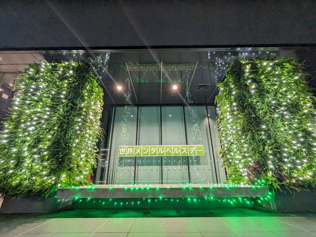 写真：市川市役所第一庁舎入口付近に世界メンタルヘルスデーの掲示を行い、その周りに白と緑の電飾でライトアップを行っている様子、正面からのアングル