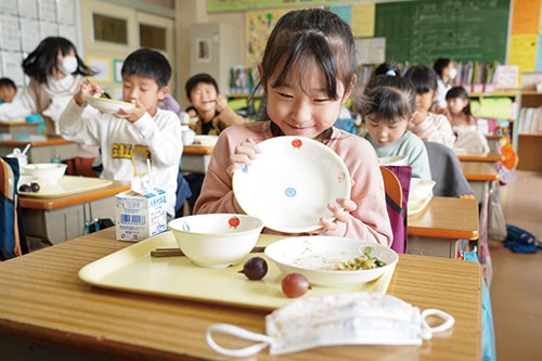 画像；市川市のシンボルマークが付いた食器を見せる子ども