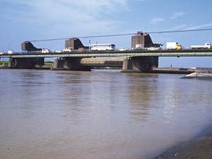 画像：ローリングゲート時代の行徳可動堰と、かつての行徳橋。中央のゲートが持ち上がっている。