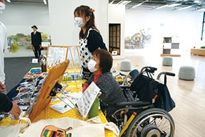 写真：接客しているエプロン姿の女性と車椅子の女性 