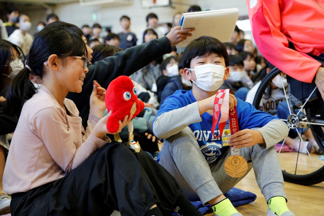 写真：貴重なメダルやパリ大会マスコット「フリージュ」の人形を持つ児童