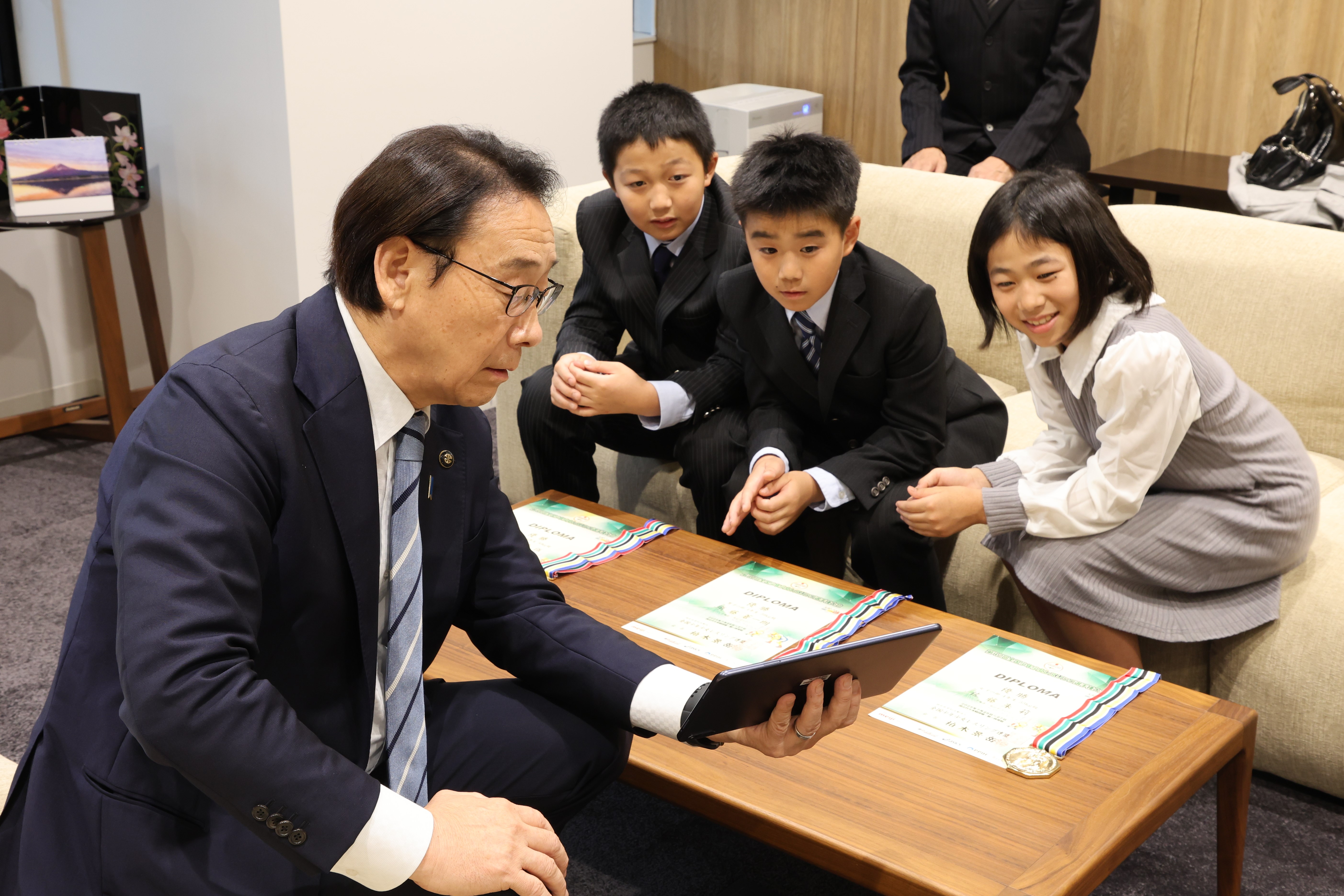 写真:タブレット端末で大会の動画を視聴する田中市長、宮藤選手、須藤選手、佐藤選手