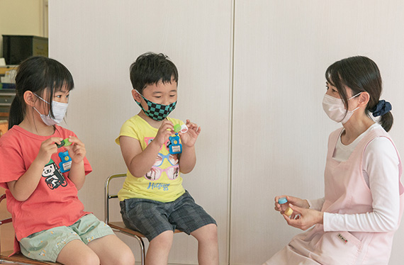 写真:ペットボトルのキャップを持った大人の女性と、女の子と男の子