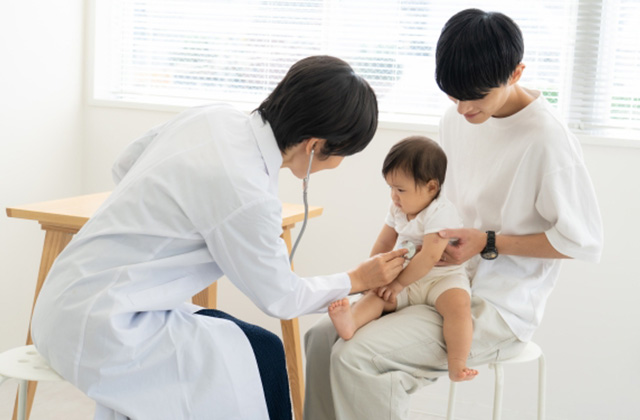 写真:子どもを抱きかかえる男性と病院の先生に聴診器を当てられている子ども